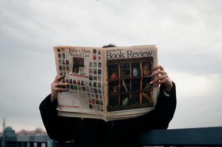 image of a person reading the newspaper featuring a book review for the beyond the twelve book review
